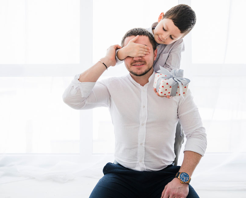 Criança com presente na mão, está a tapar olhos ao seu pai.