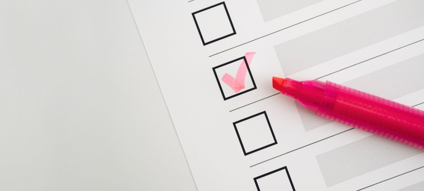 A imagem mostra uma lista de verificação com várias caixas de seleção vazias. Uma das caixas de seleção está marcada com um visto rosa, e há uma caneta marca-texto rosa ao lado, indicando que o visto foi feito com essa caneta. A imagem representa o conceito de completar tarefas ou itens em uma lista.